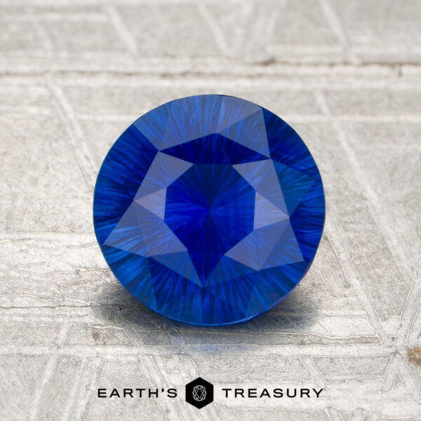 1.73-Carat Sapphire (Heated) A 1.73-carat heated sapphire, round and faceted, stands upright on a textured gray surface with "EARTH'S TREASURY" at the bottom.