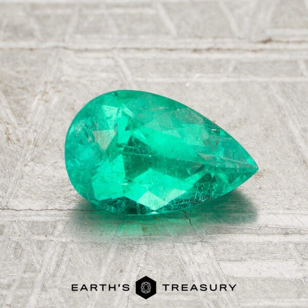 1.16-Carat Colombia Emerald (Oiled) A 1.16-carat Colombia Emerald (oiled), cut in a faceted pear shape, is showcased on a textured gray surface with the "Earth's Treasury" logo at the bottom.