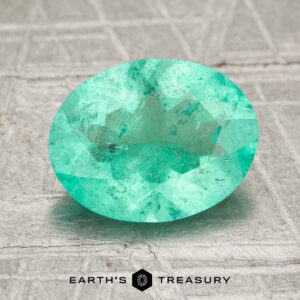 A 1.68-carat oval-cut Colombia emerald (oiled) displayed on a textured surface with the "Earth's Treasury" logo at the bottom.