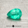 A faceted pear-shaped 0.92-carat Colombia emerald (oiled) rests on a textured gray surface, with "EARTH'S TREASURY" and a hexagonal logo displayed at the bottom.
