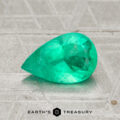 A 0.99-carat pear-shaped Colombia emerald (oiled) rests on a textured gray surface with the "Earth's Treasury" logo beneath it.