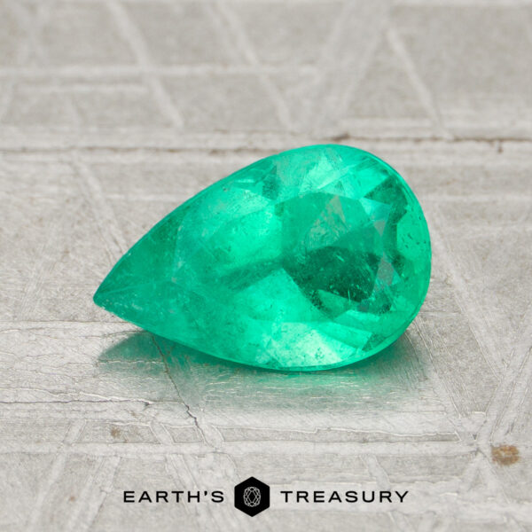 0.99-Carat Colombia Emerald (Oiled) A 0.99-carat pear-shaped Colombia emerald (oiled) rests on a textured gray surface with the "Earth's Treasury" logo beneath it.