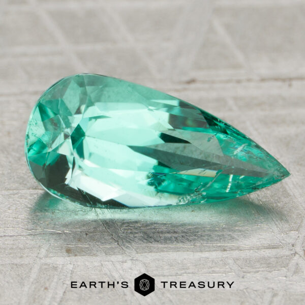1.39-Carat Colombia Emerald (Oiled) A 1.39-carat faceted, pear-shaped Colombia emerald (oiled) is displayed on a textured metallic surface with "Earth's Treasury" below.