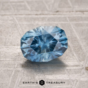 A beautiful 1.59-carat Montana Sapphire (Heated) is displayed on a textured surface with the "Earth's Treasury" logo at the bottom.
