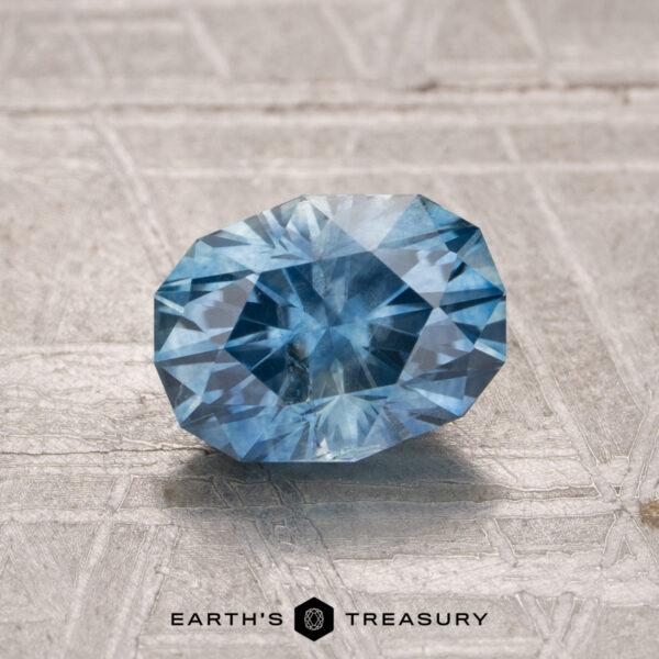1.59-Carat Montana Sapphire (Heated) A beautiful 1.59-carat Montana Sapphire (Heated) is displayed on a textured surface with the "Earth's Treasury" logo at the bottom.
