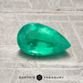 A faceted pear-shaped 0.80-carat Colombia emerald (oiled) rests on a textured surface, with "EARTH'S TREASURY" and a hexagon logo at the bottom.