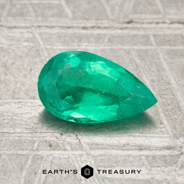 0.80-Carat Colombia Emerald (Oiled) A faceted pear-shaped 0.80-carat Colombia emerald (oiled) rests on a textured surface, with "EARTH'S TREASURY" and a hexagon logo at the bottom.