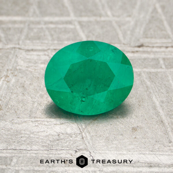 0.70-Carat Colombia Emerald (Oiled) A 0.70-carat Colombia emerald (oiled), faceted and green, rests on a textured metallic surface with "EARTH'S TREASURY" at the bottom.