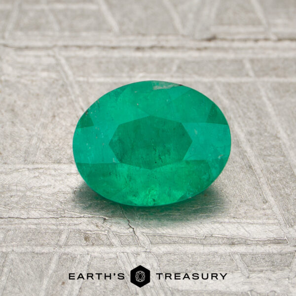 0.75-Carat Colombia Emerald (Oiled) A 0.75-carat Colombia emerald (oiled), oval-cut, is displayed on a textured gray surface with "EARTH'S TREASURY" at the bottom.