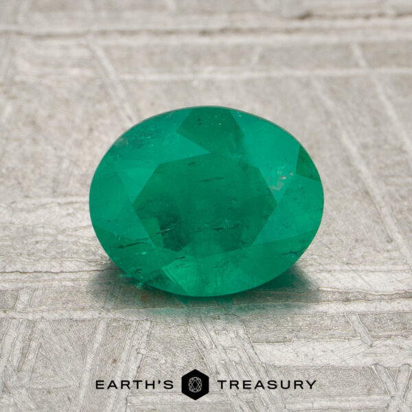 A 1.05-carat Colombia emerald (oiled) in an oval cut is displayed on a textured surface, with the Earth’s Treasury logo and text at the bottom.