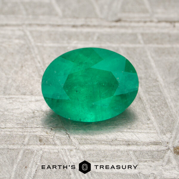 0.81-Carat Colombia Emerald (Oiled) A 0.81-carat oval-cut Colombia emerald (oiled) rests on a textured metallic surface, with "EARTH'S TREASURY" displayed at the bottom.