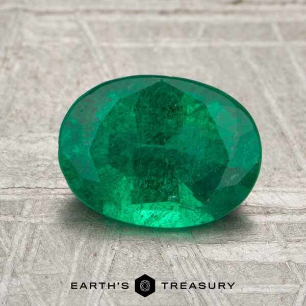 1.40-Carat Zambia Emerald (Oiled) A 1.40-carat Zambia emerald (oiled) in an oval cut is displayed on a textured surface, with "Earth's Treasury" and a hexagon logo beneath it.