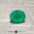 A 0.44-carat Colombia Emerald (oiled), oval-shaped and green, is displayed on a textured silvery surface with "EARTH'S TREASURY" at the bottom.