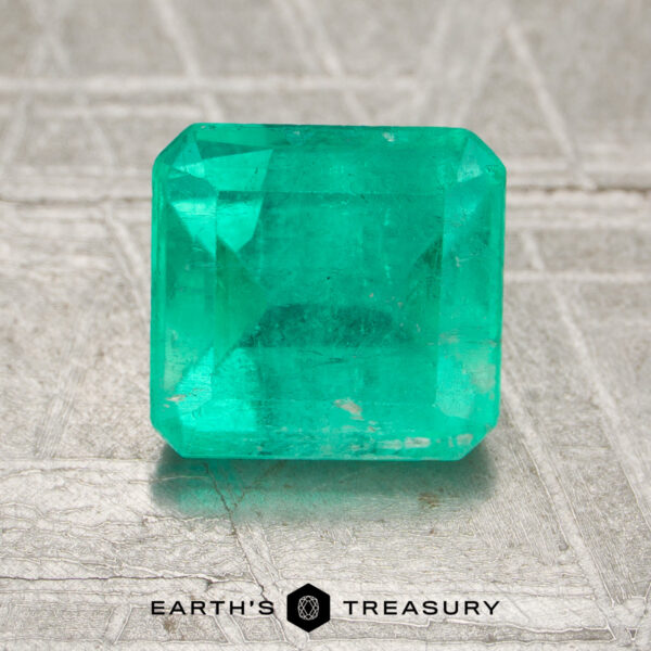 1.65-Carat Colombia Emerald (Oiled) A 1.65-carat oiled Colombia emerald with a rectangular cut is displayed on a textured surface, featuring the "Earth's Treasury" logo and text at the bottom of the image.