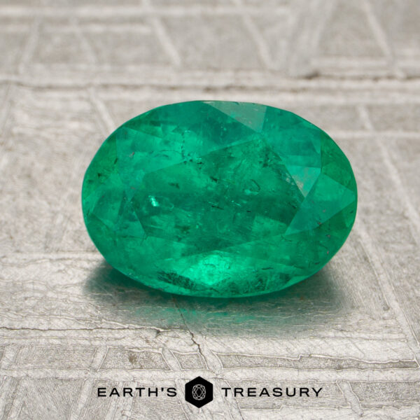 1.36-Carat Colombia Emerald (Oiled) A 1.36-carat Colombia emerald (oiled), oval-cut, is displayed on a textured metallic surface with the "Earth's Treasury" logo beneath.