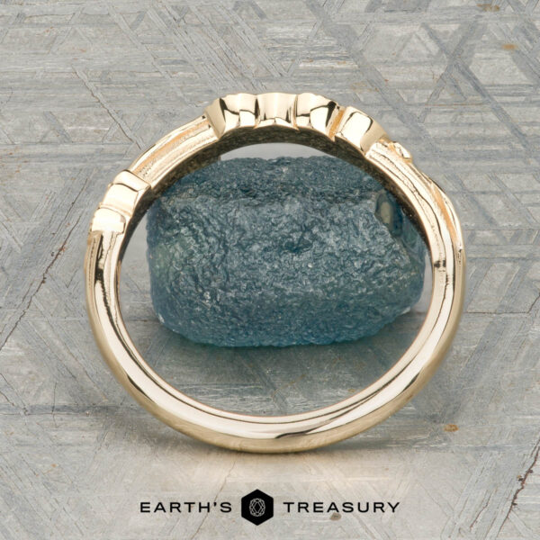 The "Amborella" band in 14K yellow gold The "Amborella" band in 14K yellow gold with leaf and diamond accents is shown on a rough blue gemstone, with the "Earth's Treasury" logo and text below.