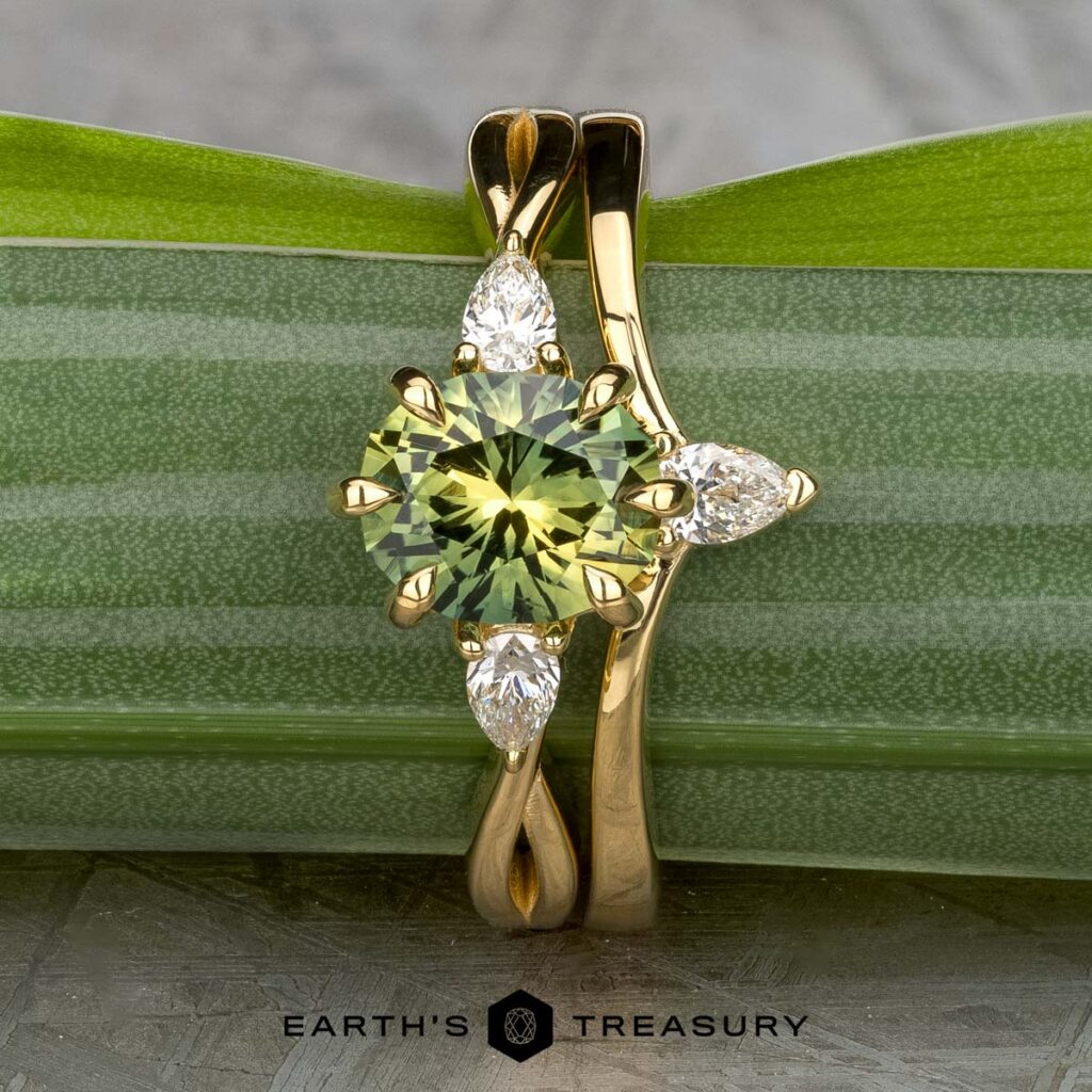 The Soriano, Rafael 1 & 2 ring features a round green gemstone and three pear-shaped clear stones, showcased on a green leaf with The Earth’s Treasury logo at the bottom, capturing the elegance of women’s wedding bands.