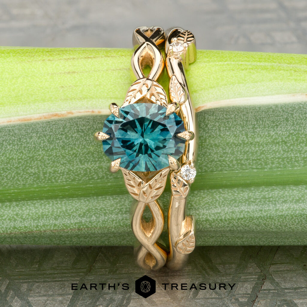 The Cavendish teal gemstone ring with leaf and vine details is paired with the Rio gold women’s wedding band, both displayed on a green stem. The Earth’s Treasury logo appears at the bottom.