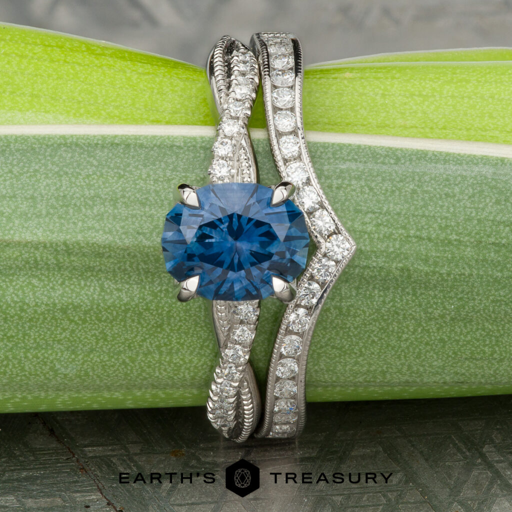The "Stacked from 39 images. Method=B (R=14,S=2)" blue gemstone ring with a diamond-studded band is paired with a matching women's wedding band, both showcased on a green stem above the Earth's Treasury logo.