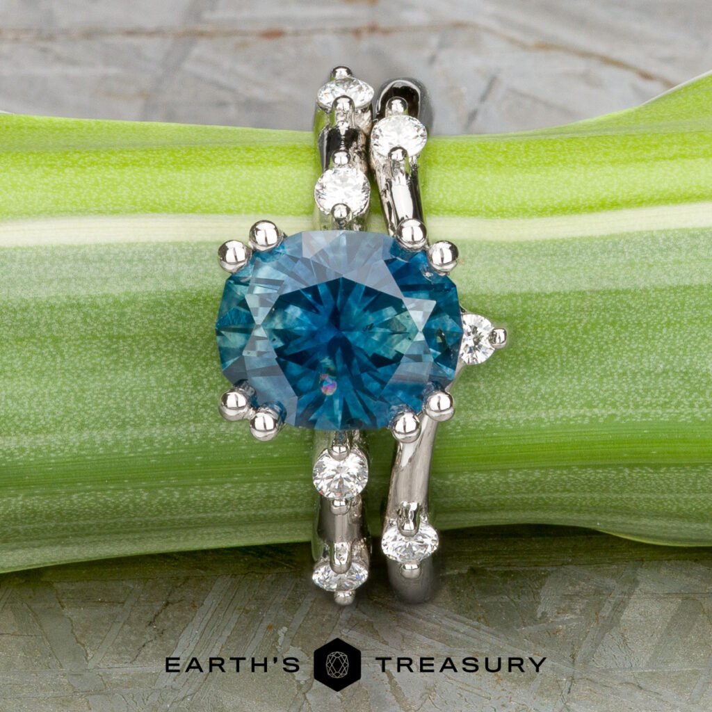 The "Pirouette" ring, crafted in platinum with a 2.46-carat Montana sapphire, is displayed on a green stem above the "Earth's Treasury" logo.