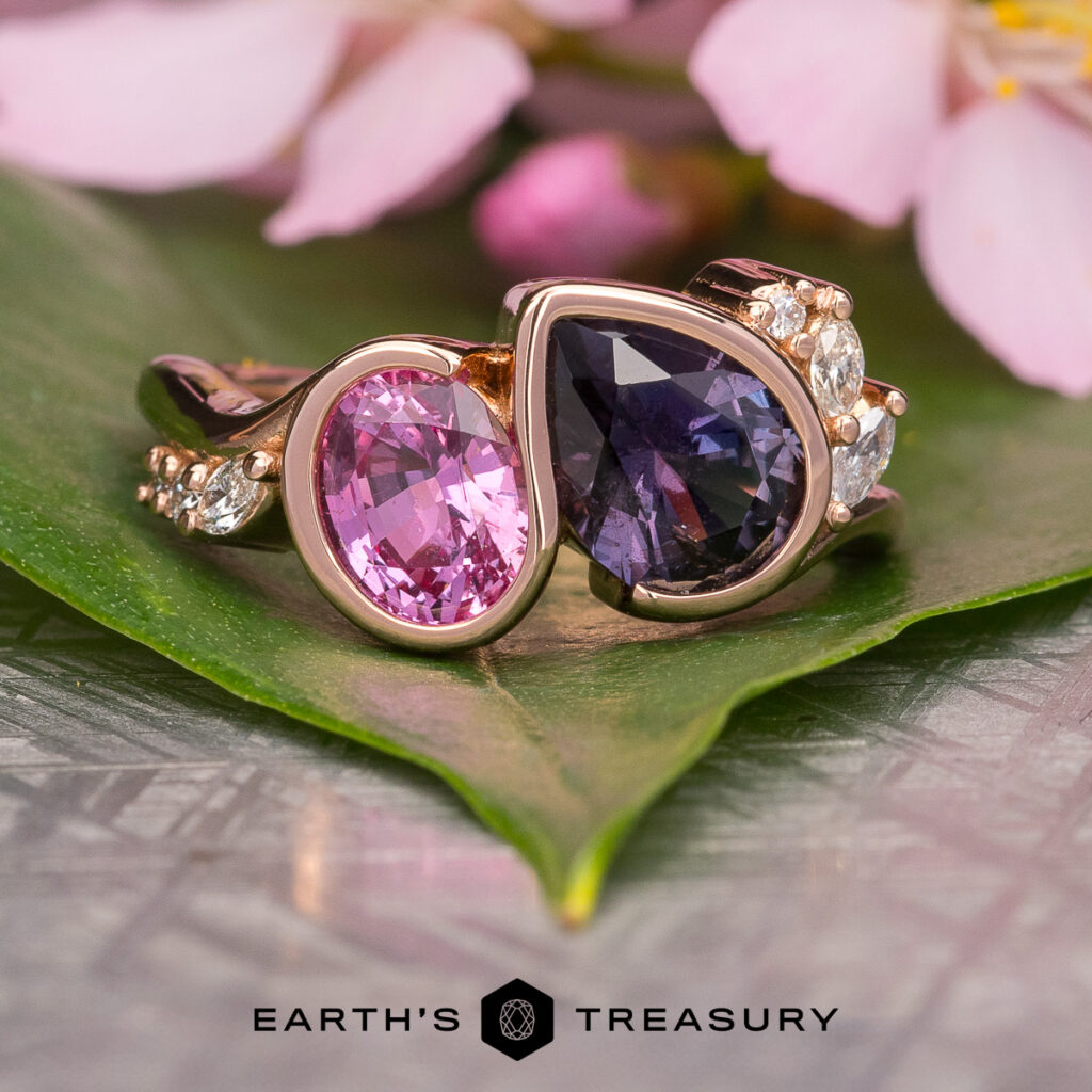 Two gold rings by Larson, Janie feature pink and dark purple gemstones with diamond accents. Displayed on a green leaf amid pink flowers. Text: "Earth's Treasury.