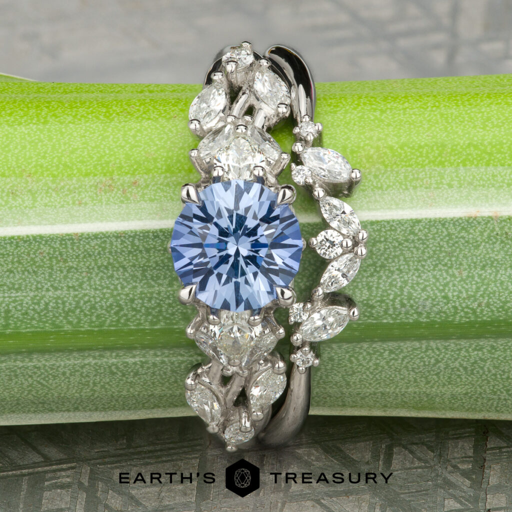 The "Stacked from 36 images. Method=B (R=14,S=2)" ring features a round blue gemstone and marquise-cut clear stones, ideal for women's wedding bands, resting on a green stem with the "Earth's Treasury" logo below.