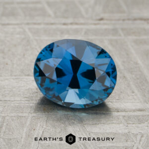 A 1.64-carat unheated sapphire with an oval cut is showcased on a textured gray surface, featuring the text "Earth's Treasury" and a logo beneath.