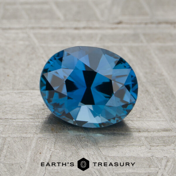 1.64-Carat Medium Blue Madagascar Sapphire (Unheated) A 1.64-carat unheated sapphire with an oval cut is showcased on a textured gray surface, featuring the text "Earth's Treasury" and a logo beneath.