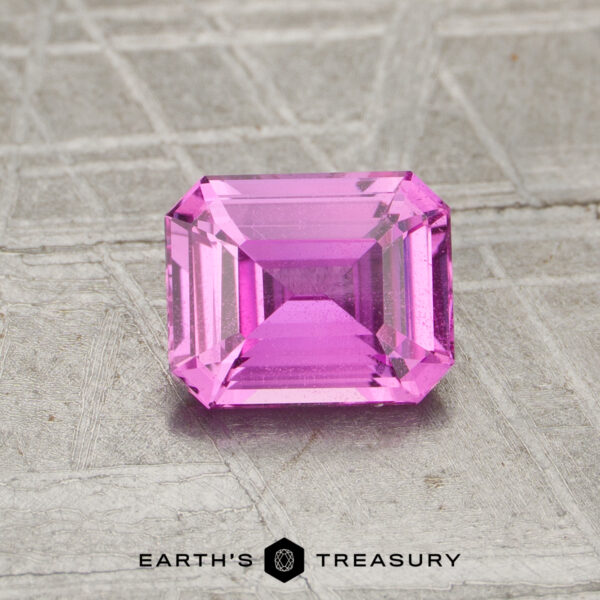 1.15-Carat Hot Pink Madagascar Sapphire (Unheated) A rectangular, step-cut pink 1.15-carat unheated sapphire rests on a textured gray surface with the text "EARTH'S TREASURY" at the bottom.