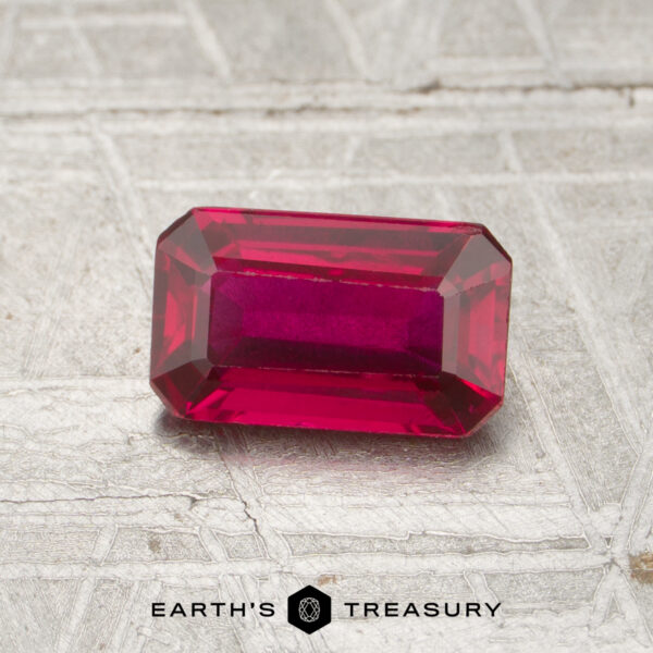 1.13-Carat Mozambique Ruby (Heated) A 1.13-carat, emerald-cut ruby rests on a textured surface with "EARTH'S TREASURY" and a hexagonal logo below.