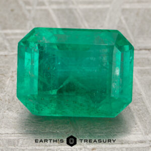 A 5.07-carat rectangular emerald gemstone with visible inclusions rests on a textured surface, the Earth's Treasury logo displayed beneath it.