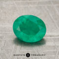 A faceted oval green 7.60-carat emerald gemstone displayed on a textured metallic surface, with the "Earth's Treasury" logo and text at the bottom.