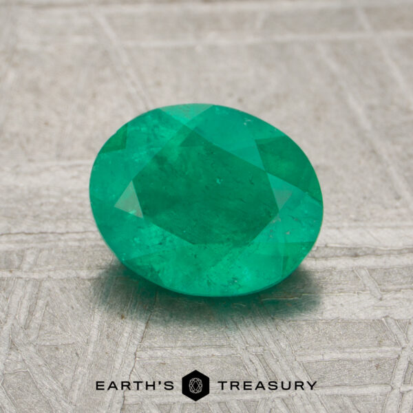 0.98-Carat Rich Green Colombian Emerald (Oiled) A faceted oval green 7.60-carat emerald gemstone displayed on a textured metallic surface, with the "Earth's Treasury" logo and text at the bottom.