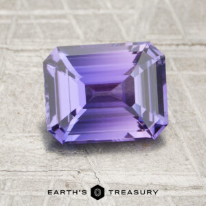 A 2.09-carat unheated Sapphire, rectangular and faceted with a purple hue, displayed on a textured light background with "Earth's Treasury" written beneath.