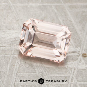 A rectangular, peack pink 2.05-carat unheated sapphire with beveled edges rests on a textured metallic surface. "EARTH’S TREASURY" is printed at the bottom of the image.