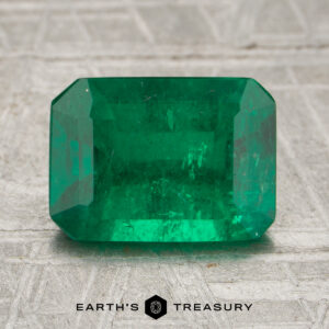 A 2.02-carat emerald gemstone with a rectangular, faceted cut rests on a textured surface, displaying the words "Earth's Treasury" below.