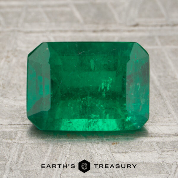 2.02-Carat Rich Green Zambian Emerald (Oiled) A 2.02-carat emerald gemstone with a rectangular, faceted cut rests on a textured surface, displaying the words "Earth's Treasury" below.