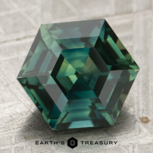 A precision-cut hexagonal 4.53-carat sapphire sits on a textured surface, with the Earth's Treasury logo and name displayed at the bottom.