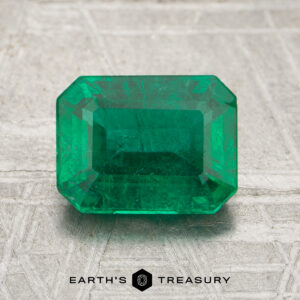 A 1.72-carat emerald-cut green gemstone is displayed on a textured surface with the Earth's Treasury logo beneath it.