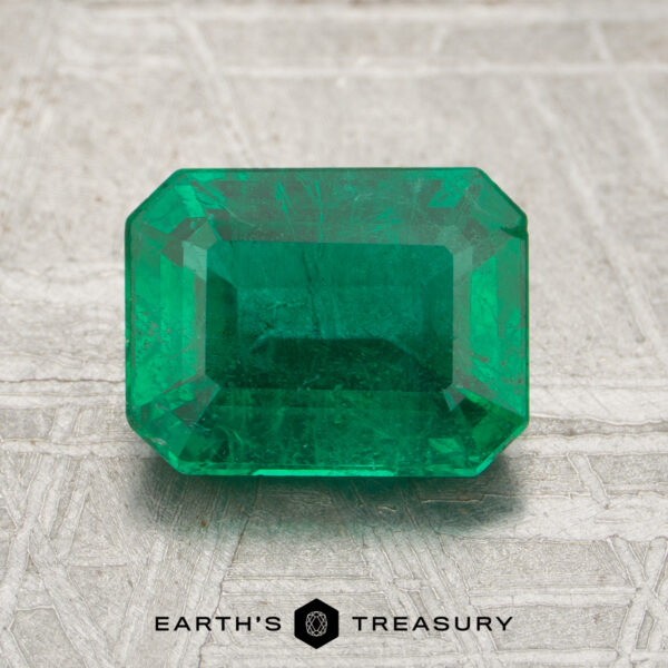 1.72-Carat Rich Green Zambian Emerald (Oiled) A 1.72-carat emerald-cut green gemstone is displayed on a textured surface with the Earth's Treasury logo beneath it.
