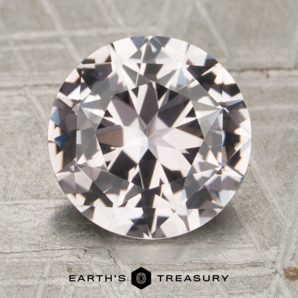 3.48-Carat Sapphire A 3.48-carat round brilliant-cut sapphire is displayed on a light, patterned surface with the text "Earth's Treasury" and a logo beneath it.