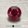 A 1.50-carat round, faceted deep red ruby is displayed on a textured surface with the words "EARTH'S TREASURY" and a hexagon logo beneath it.