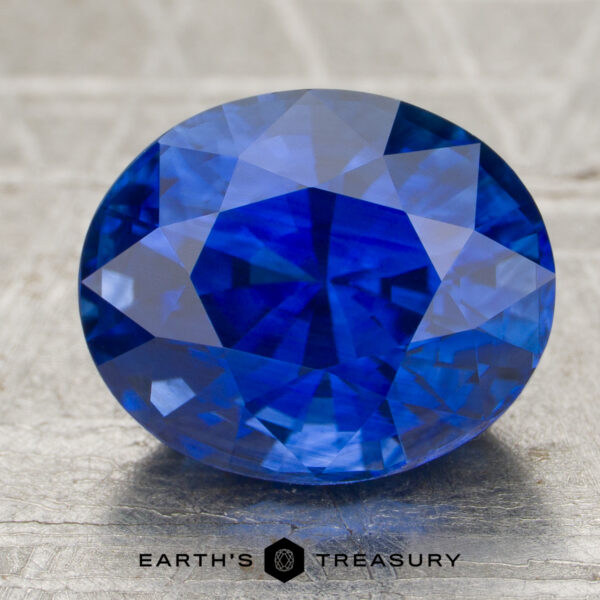 3.12-Carat Sapphire A 3.12-carat faceted oval blue sapphire is displayed on a textured surface, with the "Earth's Treasury" logo and text visible underneath.