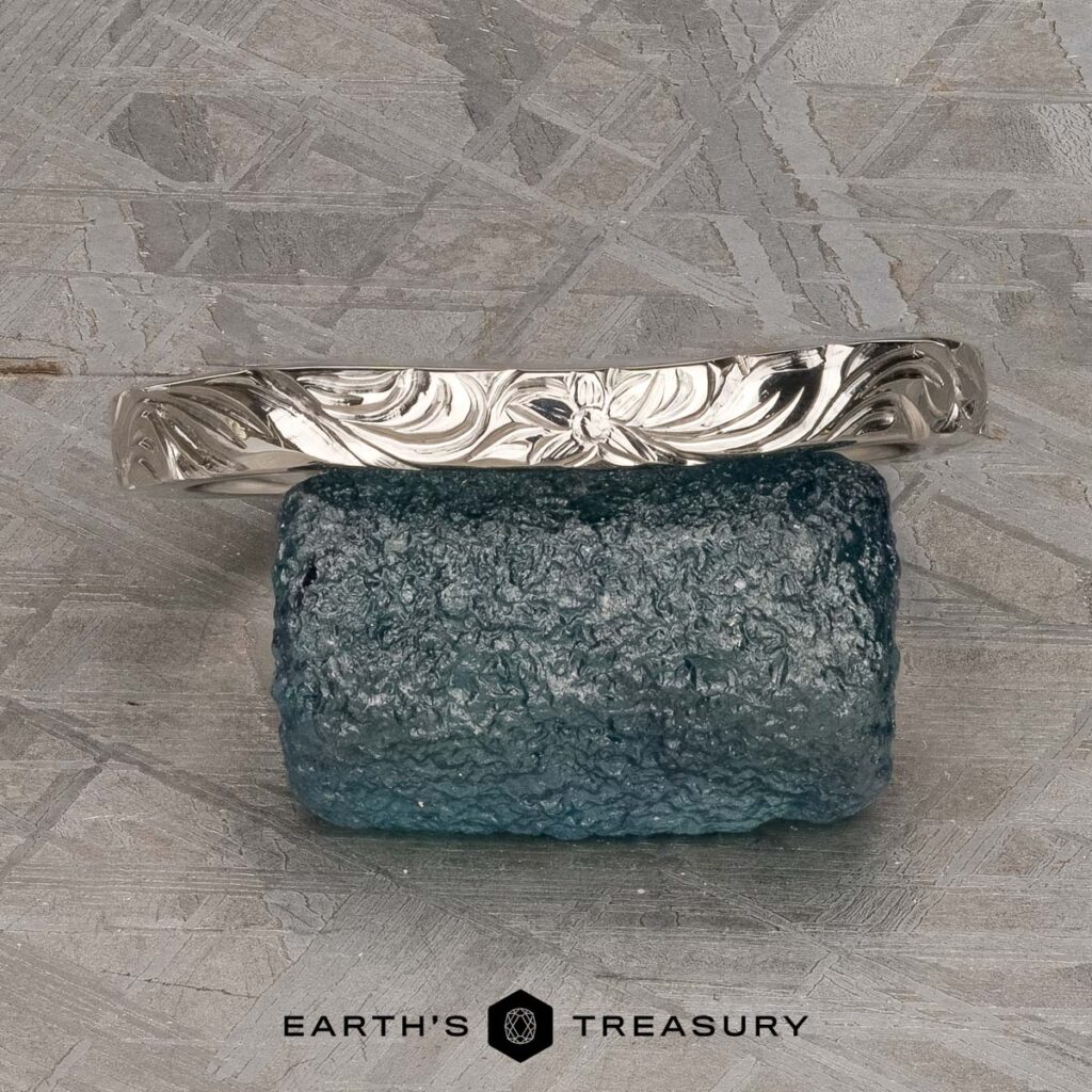 The Ravary, Riley and Van Oostenburg, Max 3 ring is shown upright on a rough blue-green glass-like stone, with the Earth's Treasury logo displayed below.