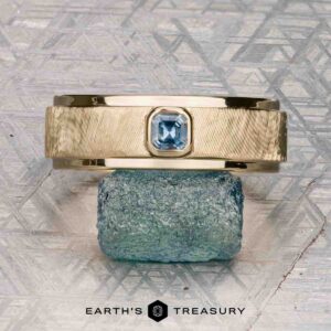 The "Montserrat" ring in 14K yellow gold with teal sapphire is shown on a rough blue stone, Earth's Treasury logo below. Ready to ship.