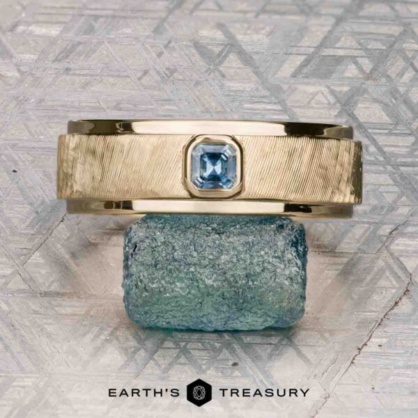 The "Montserrat" ring in 14K yellow gold with teal sapphire The "Montserrat" ring in 14K yellow gold with teal sapphire is shown on a rough blue stone, Earth's Treasury logo below. Ready to ship.