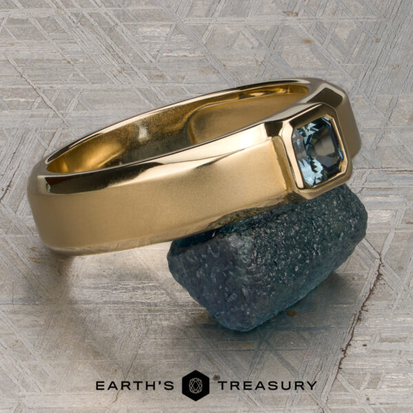 Stacked from 49 images. Method=B (R=7,S=2) Stacked from 49 images. Method=B (R=7,S=2) in 14K Yellow Gold, showcasing a rectangular blue gemstone resting on a rough stone atop a textured metallic surface. "Earth's Treasury" logo and text appear at the bottom. Ready to Ship for your convenience.
