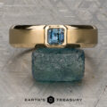 A gold ring with an emerald-cut blue gemstone, named "Stacked from 47 images. Method=B (R=7,S=2)," is displayed balanced atop a raw blue stone against a textured metallic backdrop. Crafted in 14K yellow gold and Ready to Ship, the Earth’s Treasury logo appears at the bottom.