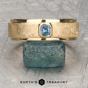 A gold textured ring named "Stacked from 49 images. Method=B (R=7,S=2)" with a square blue gemstone in a Florentine Finish is displayed on a rough blue stone. The text "Earth's Treasury" appears at the bottom.