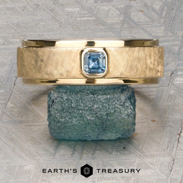 Stacked from 49 images. Method=B (R=7,S=2) A gold textured ring named "Stacked from 49 images. Method=B (R=7,S=2)" with a square blue gemstone in a Florentine Finish is displayed on a rough blue stone. The text "Earth's Treasury" appears at the bottom.